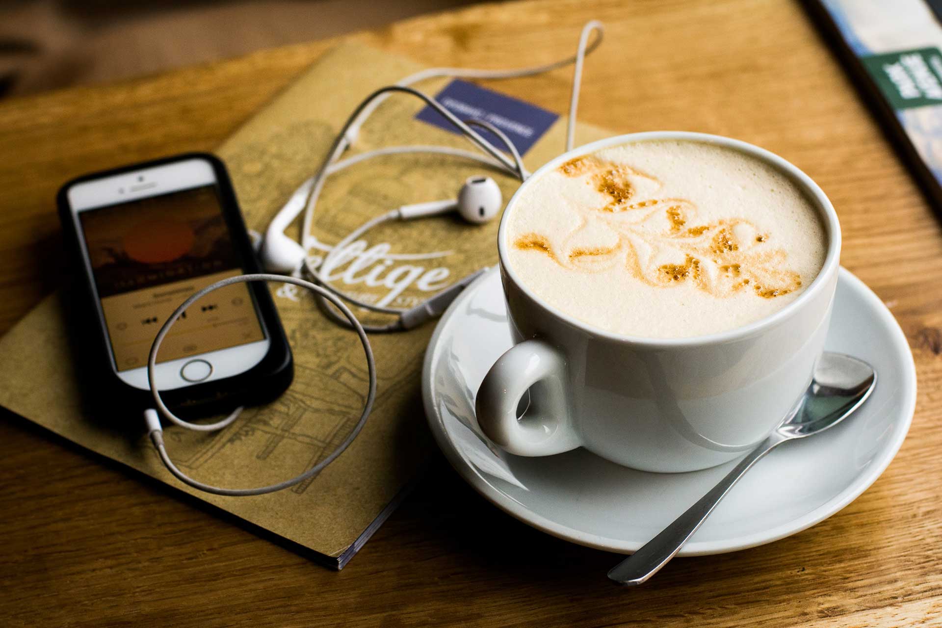 Phone with headphones attached and a coffee on a table