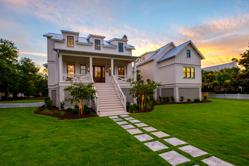 side view of 2 story elevated white home, concrete stone pathway leading up to front porch and lush grass